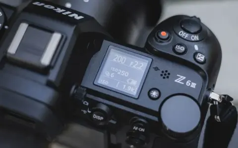 Górna część aparatu Nikon Z6 III z widocznym ekranem LCD, pokrętłem trybów i przyciskiem nagrywania.