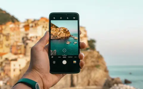 Dłoń trzyma smartfon, na ekranie którego widać malowniczą włoską wioskę nad morzem. Chcesz wiedzieć, jak ulepszyć aparat w telefonie? Oto przykład pięknego ujęcia!