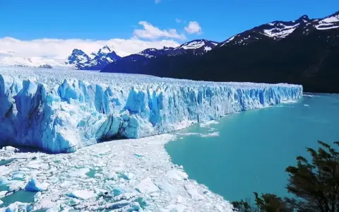 Impresionante glaciar Perito Moreno, con sus paredes de hielo azul intenso y el agua turquesa del lago. Montañas nevadas al fondo.