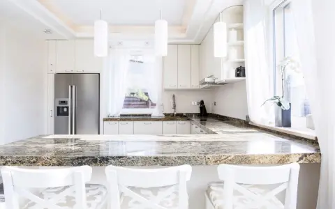 Plan de travail en granit, un danger potentiel pour les couteaux de cuisine. Cuisine moderne avec réfrigérateur, armoires blanches et tabourets.