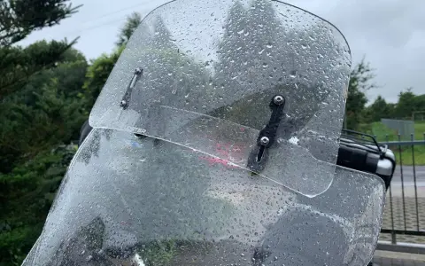 Przednia szyba motocykla pokryta kroplami deszczu, z widocznymi mocowaniami.