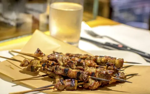 Arrosticini, uno dei piatti tipici abruzzesi, serviti su carta paglia con un bicchiere di vino bianco sullo sfondo.
