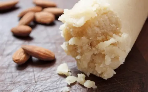 Frische Mandeln liegen neben einer Rolle Marzipan Rohmasse, bereit zum Verarbeiten.