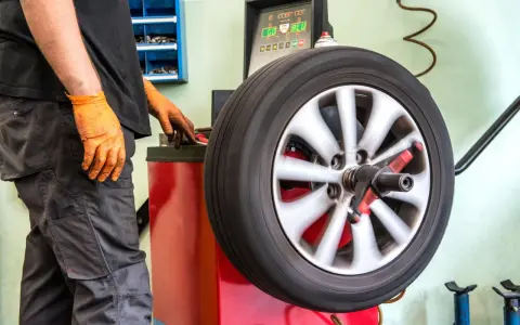 Meccanico con guanti arancioni controlla la vibrazione auto semiasse su una macchina bilanciatrice.