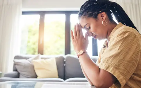 A woman with braided hair and hoop earrings prays with her hands clasped, finding peace during her christian prayer times.