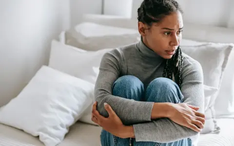 Donna seduta sul letto, abbracciata, con espressione preoccupata. Sembra soffrire di ansia da separazione dal partner.