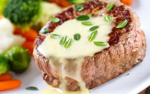 Un steak tendre nappé d'une onctueuse sauce béarnaise, accompagné de légumes verts et de carottes.