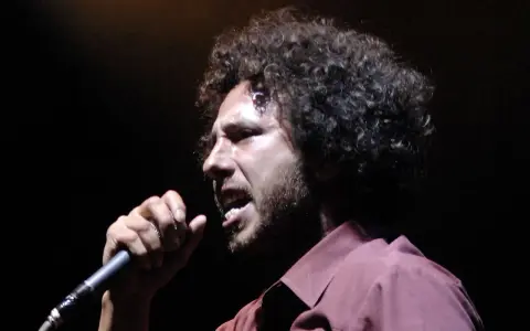 Zack de la Rocha heute, mit seinem charakteristischen lockigen Haar und einem Mikrofon in der Hand, singt leidenschaftlich auf der Bühne.