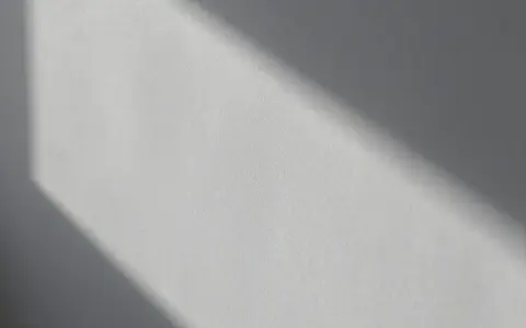 Światło podkreśla nierówności na elewacji, tworząc cień o geometrycznym kształcie.