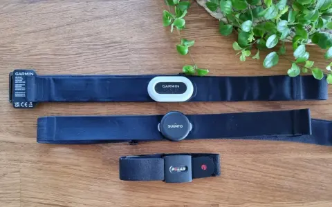 Tre pulsbands från Garmin, Suunto och Polar ligger på ett trägolv. Jämför garmin pulsband skillnad med de andra.