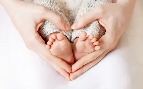 Manos formando un corazón alrededor de los pies de un bebé, evocando la protección y el complemento de maternidad con retroactividad.