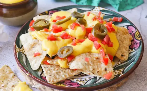 Nachos con queso derretido, jalapeños y tomate picado en un plato decorado.