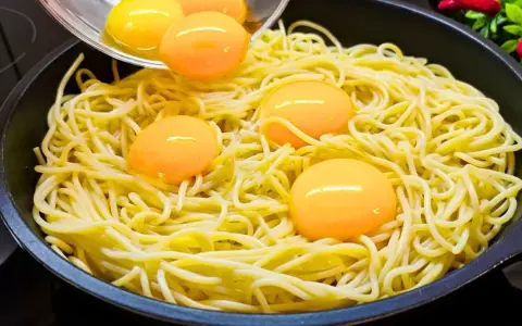 Makaron z jajkiem w patelni, żółtka tworzą złote kropki na żółtym tle.