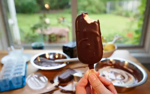 Ein abgebissener Schokoriegel, der zeigt, wie einfach es ist, Magnum Eis selber machen. Zutaten und Eisformen liegen bereit.