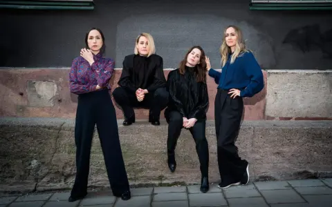 Sahara Hotnights medlemmar poserar framför en vägg. De bär mörka kläder och ser ut att vara redo för en fotografering.