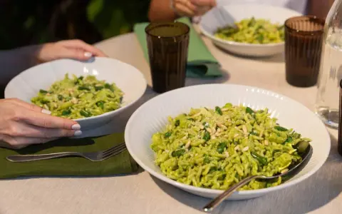 Due piatti di trofie al pesto, condite con fagiolini e pinoli, pronte per essere gustate.