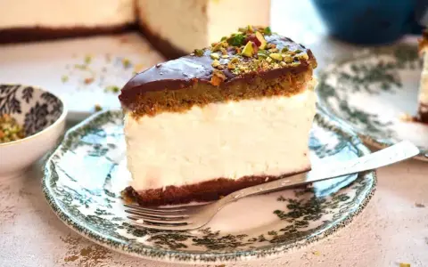 Sernik dubajski z polewą czekoladową i pistacjami, podany na ozdobnym talerzyku. Wygląda pysznie!