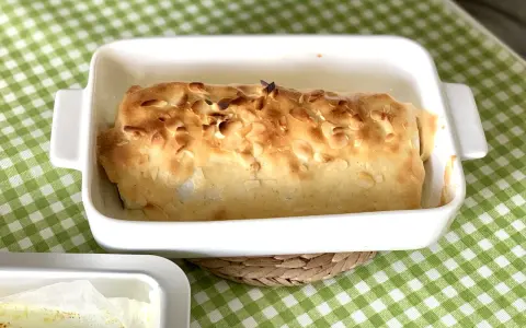Bacalao gratinado con alioli, cubierto de almendras tostadas, en una fuente blanca sobre mantel de cuadros verdes.