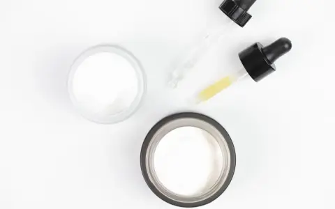 Dwa słoiczki kremu i pipetki z serum, idealne do pielęgnacji skóry głowy z kwasem salicylowym.