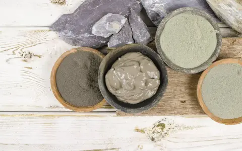 Pots de différentes argiles, dont une argile verte pour dégonfler, sur un fond en bois blanc et brut.