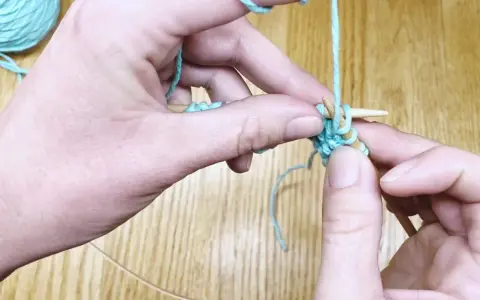 Manos tejiendo punto ojo de perdiz con hilo turquesa y agujas de madera.