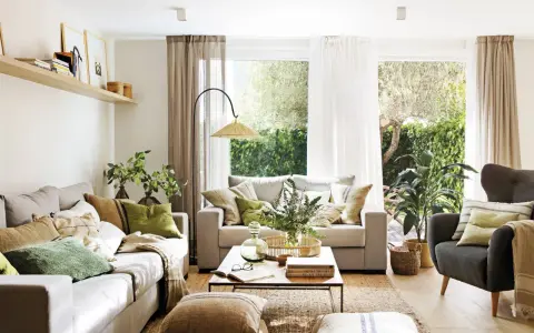 Salón con sofás, sillón, mesa de centro y alfombra de yute. La decoracion aesthetic se realza con cojines en tonos tierra y verdes, plantas y luz natural.