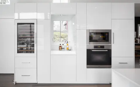 Cucina moderna bianca con elettrodomestici integrati e una porta finestra che offre una vista sul verde.