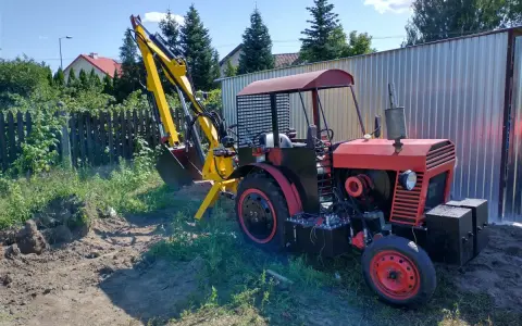 Czerwony traktor C-330 z zamontowaną żółtą koparką, gotowy do pracy w ogrodzie.