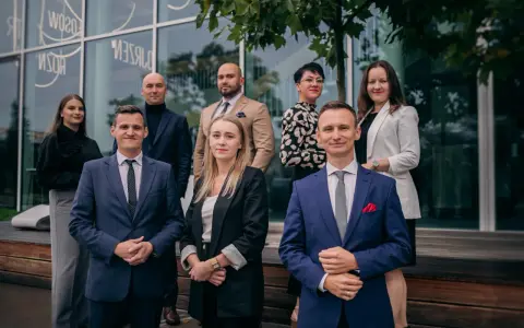 Grupa prawników w eleganckich strojach pozuje przed budynkiem.