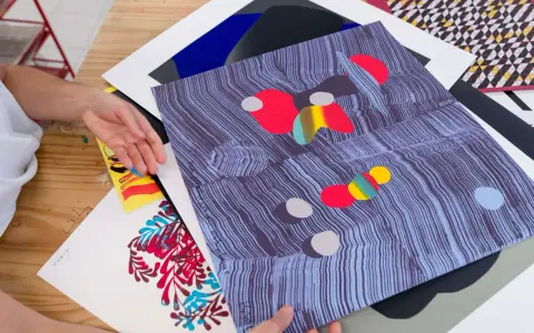 Manos revisando impresiones de arte abstracto, con vibrantes colores y patrones. El material serigrafia resalta en cada detalle.