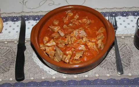 Un cuenco de barro rebosante de magro con tomate, listo para ser disfrutado con pan y vino tinto.
