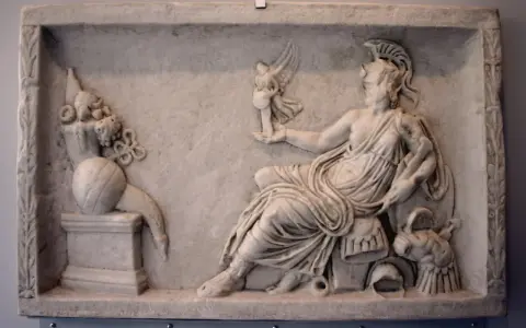 A marble relief depicting a seated figure, possibly a goddess, holding a winged victory. This scene reflects the rich tapestry of Roman paganism, with symbolic offerings and divine representation.