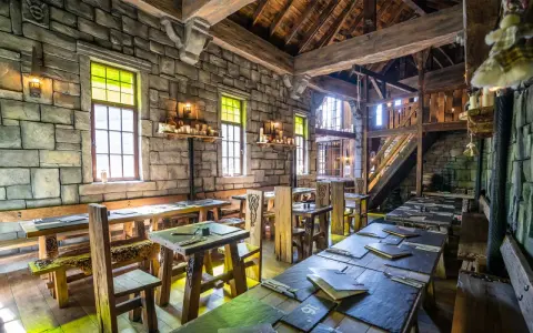 Rustikale Phantasialand Taverne mit Steinwänden, Holztischen und Bänken, Kerzenlicht und mittelalterlichem Flair.