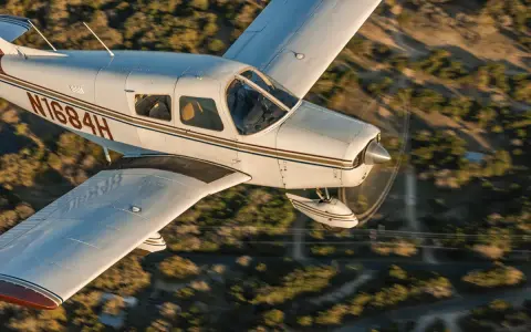 Eine Piper Cherokee 140 fliegt über eine bewaldete Landschaft.
