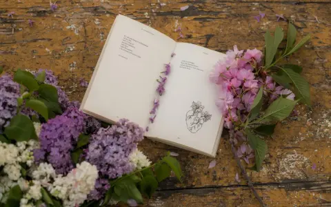 Un libro aperto con poesie d'amore passionali anonime, decorato con fiori lilla e rosa su un tavolo di legno consumato.