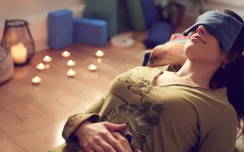 Kvinna med ögonbindel vilar under brahma yoga, omgiven av levande ljus och yogablock.