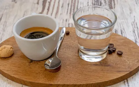 Espresso mit einem Glas Wasser, das die Aromen reinigt. Ein Keks und Kaffeebohnen vervollständigen das Bild.