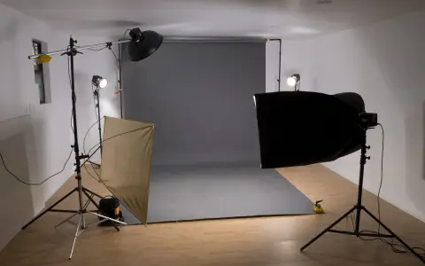 Studio fotograficzne z szarym tłem, lampami i dyfuzorem. Światło kontrowe tworzy dramatyczne cienie.