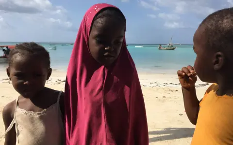 Dzieci na plaży, w tle turkusowe morze i łodzie. To obrazek z życia na Zanzibarze.