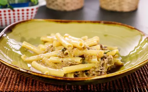 Piatto di ziti alla genovese, pasta condita con un ricco ragù di carne, servita in una ciotola verde.