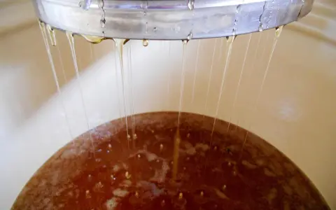 Krople płynu spływają z metalowej obręczy do brązowej powierzchni, wskazując na proces fermentacji wina i jego temperaturę.