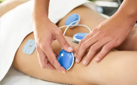 Fizykoterapia co to? Terapeuta umieszcza elektrody na nodze pacjenta, co jest częścią zabiegu.