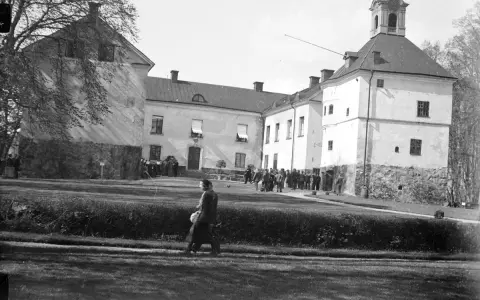 En grupp människor samlas framför Rydboholms slott. En kvinna går över gräsmattan.