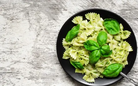 Lekkostrawny makaron farfalle z pesto i świeżą bazylią na czarnym talerzu, gotowy do podania.