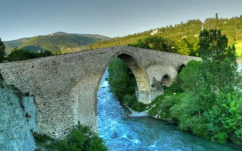 El histórico puente de San Miguel en Jaca cruza un río caudaloso rodeado de vegetación y montañas.