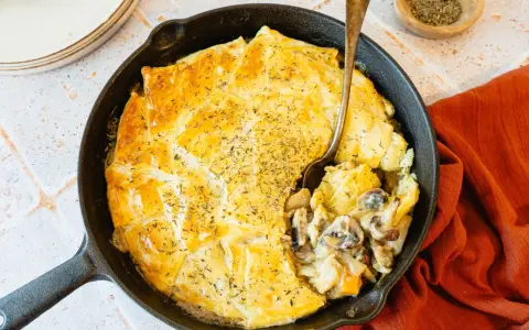 Une tourte aux champignons dorée et appétissante, servie dans une poêle en fonte, avec une cuillère prête à déguster.