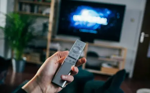 Dłoń trzymająca srebrny pilot do telewizora, na ekranie logo Universal.