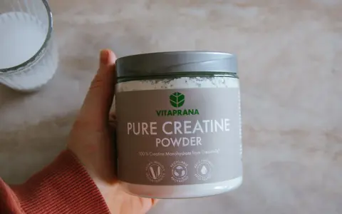 En hand håller en burk med Vitaprana Pure Creatine Powder. Kan vara ett komplement för den som vill ha **kreatin viktnedgång**.