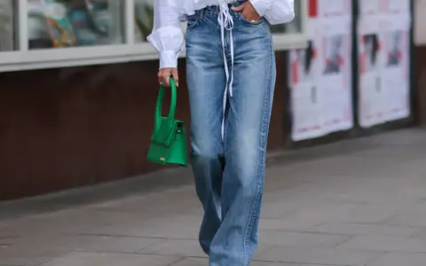 Mujer con camisa blanca y pantalones vaqueros anchos, a la altura de la cintura, con un bolso verde brillante.