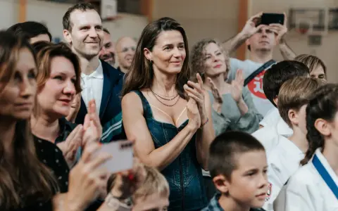 Agnieszka Grochowska z uśmiechem klaszcze, otoczona ludźmi na widowni.